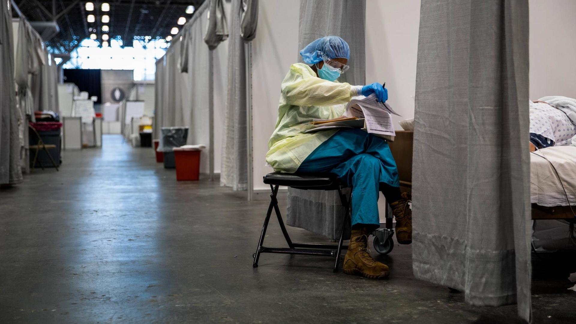 Eine medizinische Fachkraft sitzt in Schutzkleidung am Fußende einer Corona-Krankenbox in der provisorisch eingerichteten Javits New York Medical Station