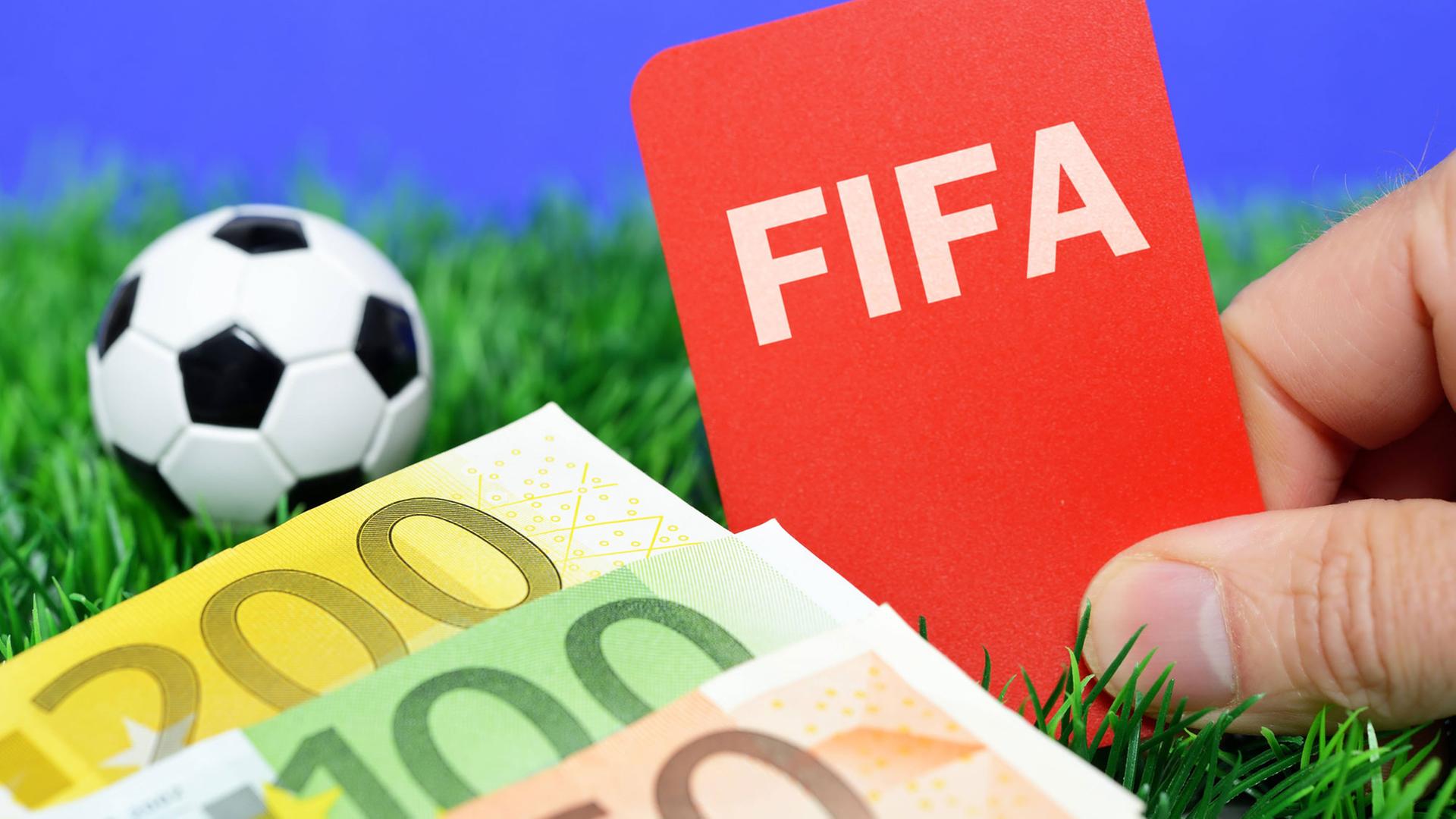 Jemand hält ein FIFA-Logo neben Geld-Scheine und einen Fußball.