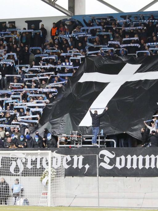 Im Fanblock des FC Chemnitz ist eine schwarze Fahne mit einem Kreuz aufgespannt. Darunter auf einem weiteren Banner "Ruhe in Frieden, Tommy"