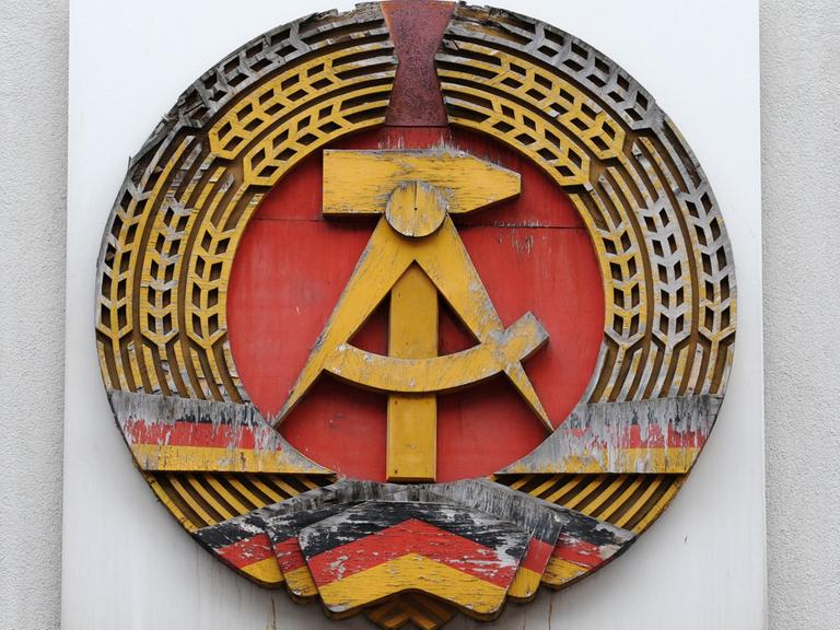 Ein DDR-Emblem hängt an einer Wand.