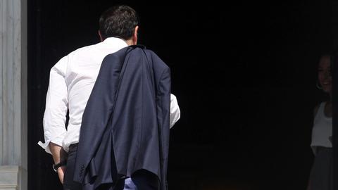 Alexis Tsipras kehrt in Athen in sein Büro zurück. Man sieht ihn von hinten, seine Jacke hängt über der Schulter.