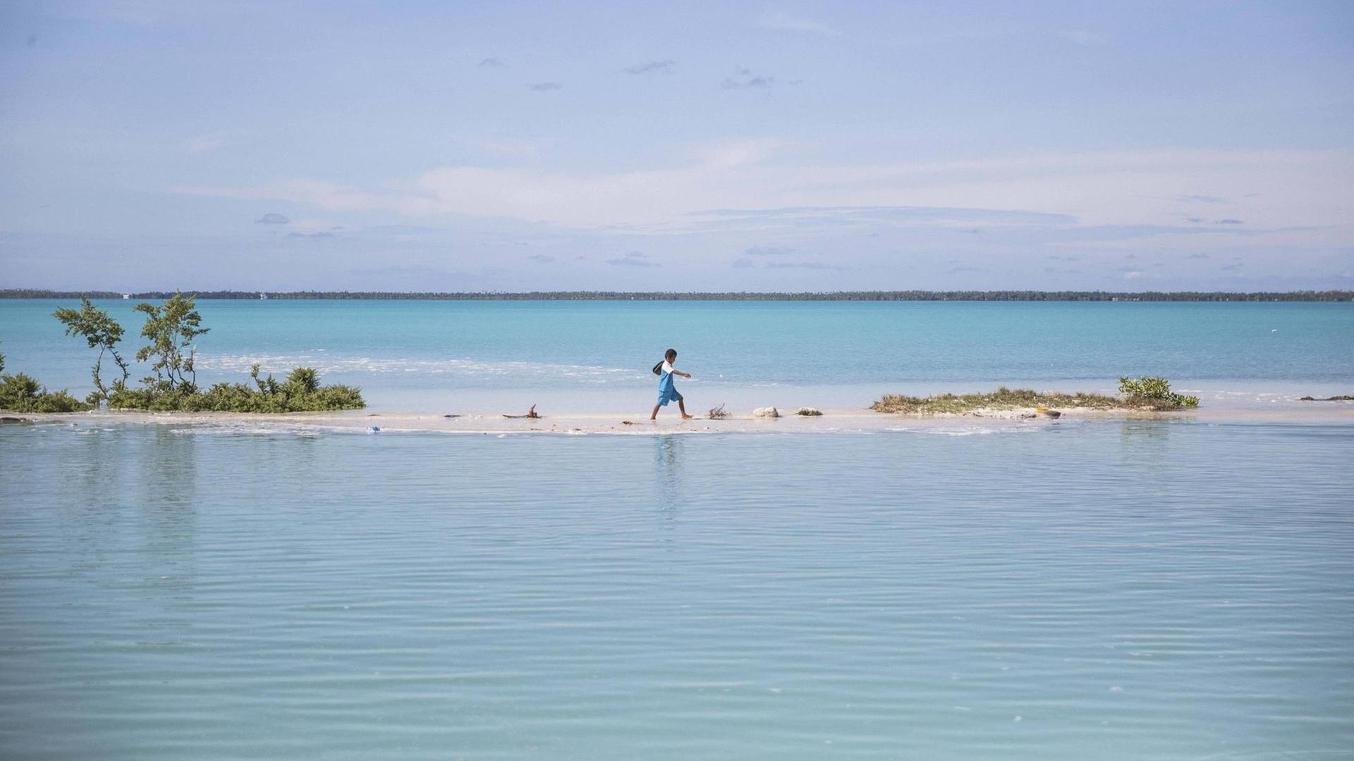 Ein Junge watet auf einer Insel des Pazifikstaates Kiribati durch eine Lagune.