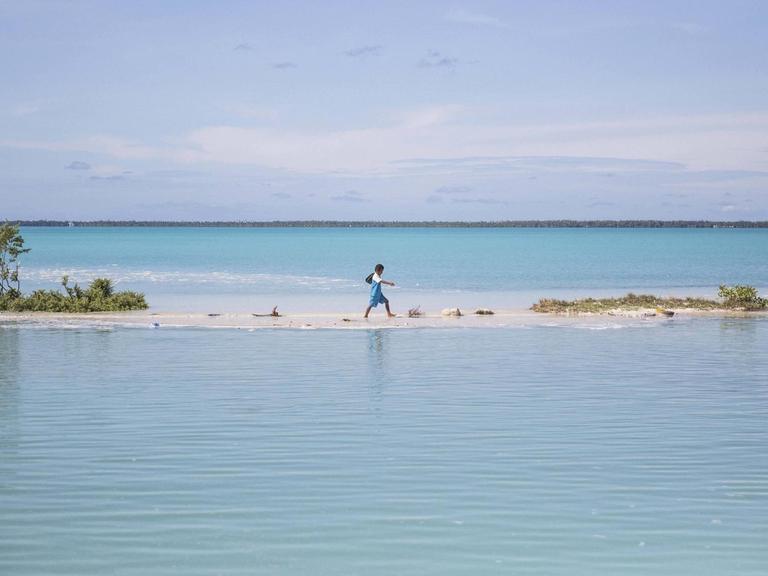 Ein Junge watet auf einer Insel des Pazifikstaates Kiribati durch eine Lagune.