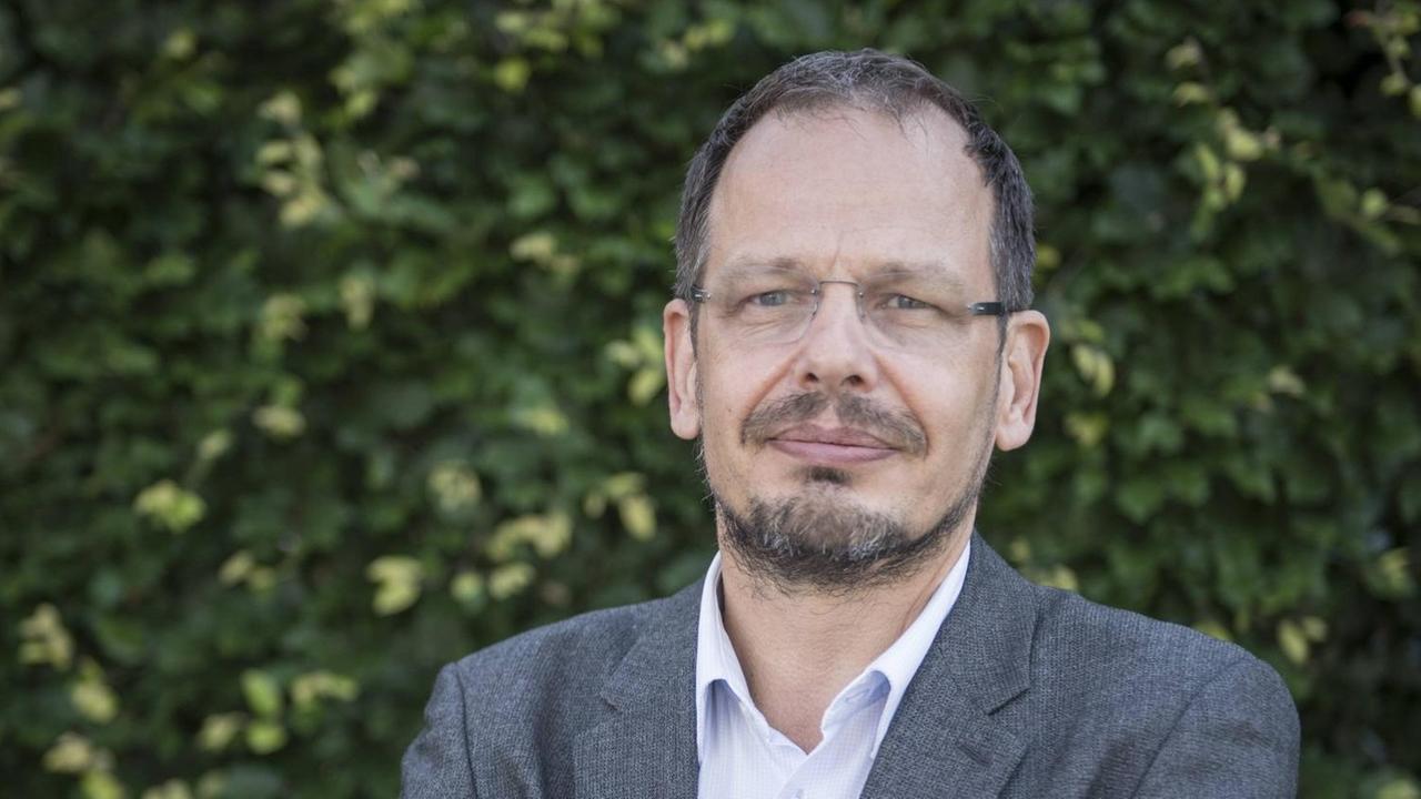 Der Journalist Hans-Joachim Seppelt posiert für ein Portrait in Berlin vor einer grünen Hecke.