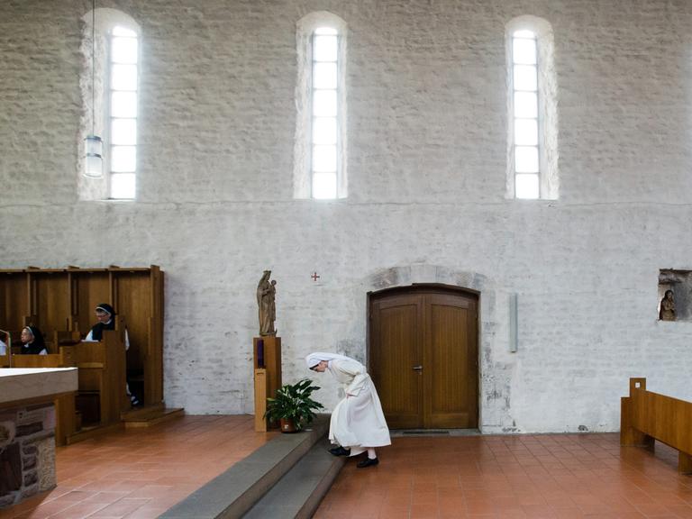 Eine Novizin verbeugt sich vor dem Altar in einer Klosterkirche.