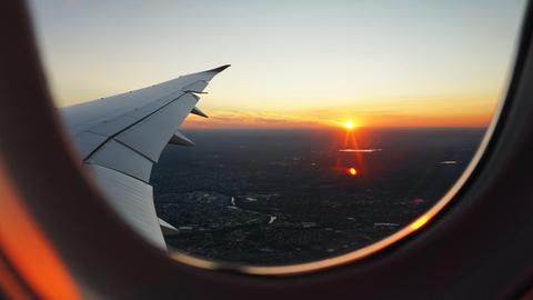 Blick aus einem Flugzeugfenster auf den Flügel und die untergehende Sonne.