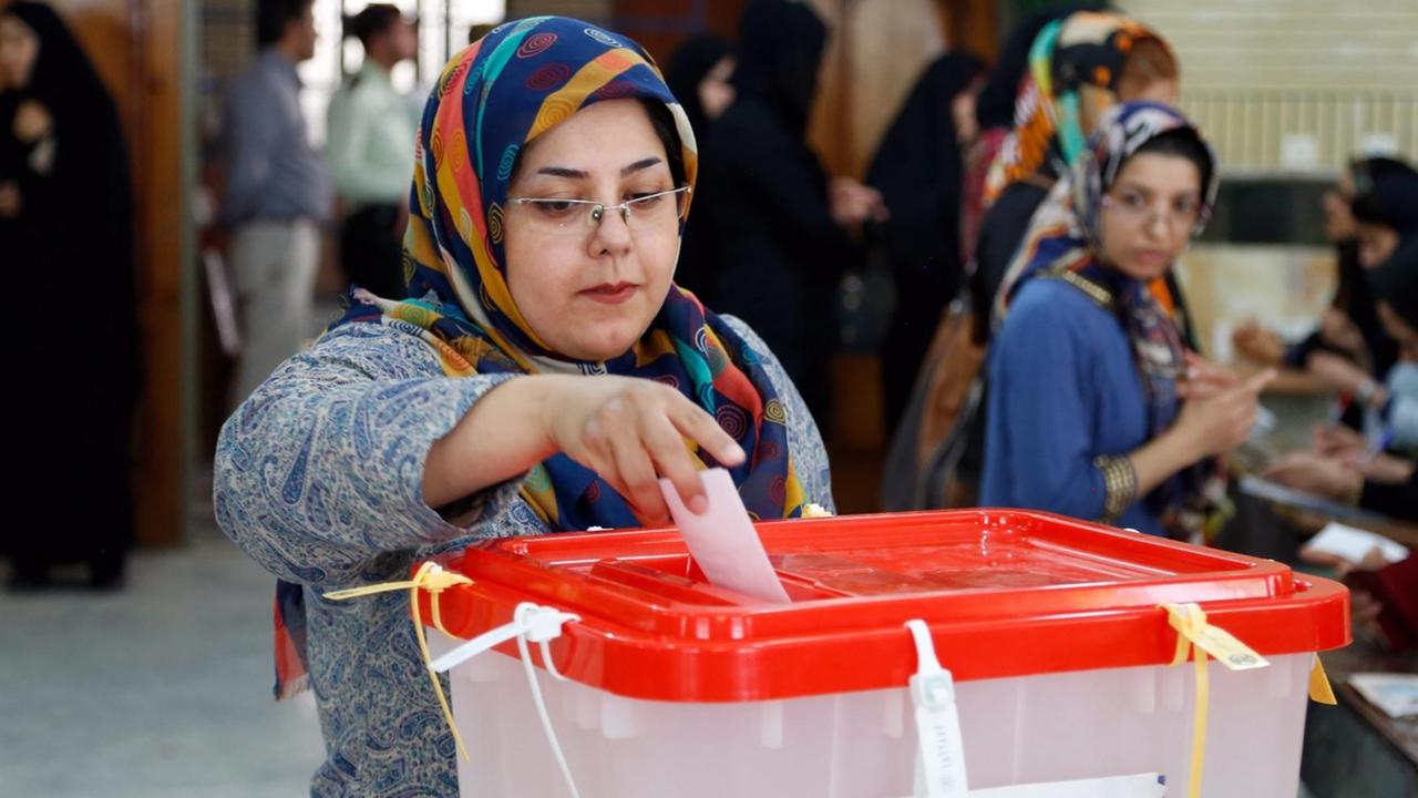 Die Frau mit Kopftuch und Brille wirft ihren Stimmzettel in einer Moschee in die Wahlbox mit rotem Deckel. Hinter ihr wählen weitere Frauen.