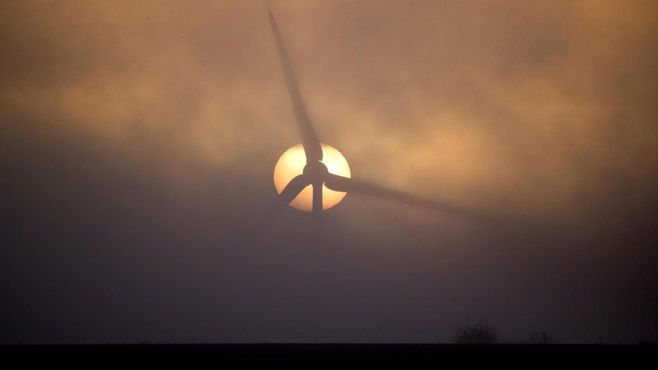 Bei Sehnde in Niedersachsen geht die Sonne hinter einem Windrad inmitten von Nebelschwaden auf