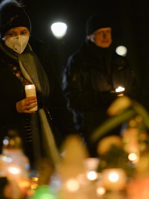 Das Foto zeigt eine gläubige Frau mit Mundschutz im Gebet. Im Vordergrund brennen Kerzen.
