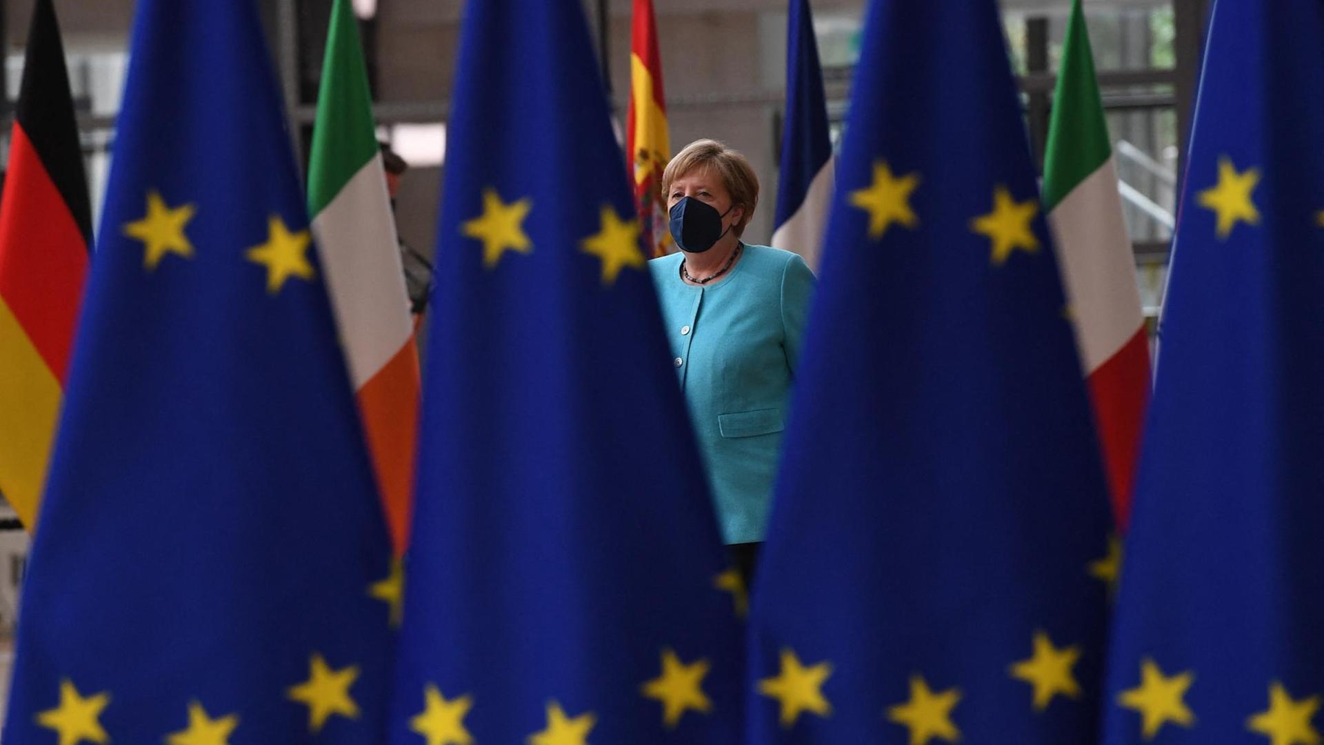 Kanzlerin Merkel geht hinter einer Reihe von EU-Flaggen entlang.