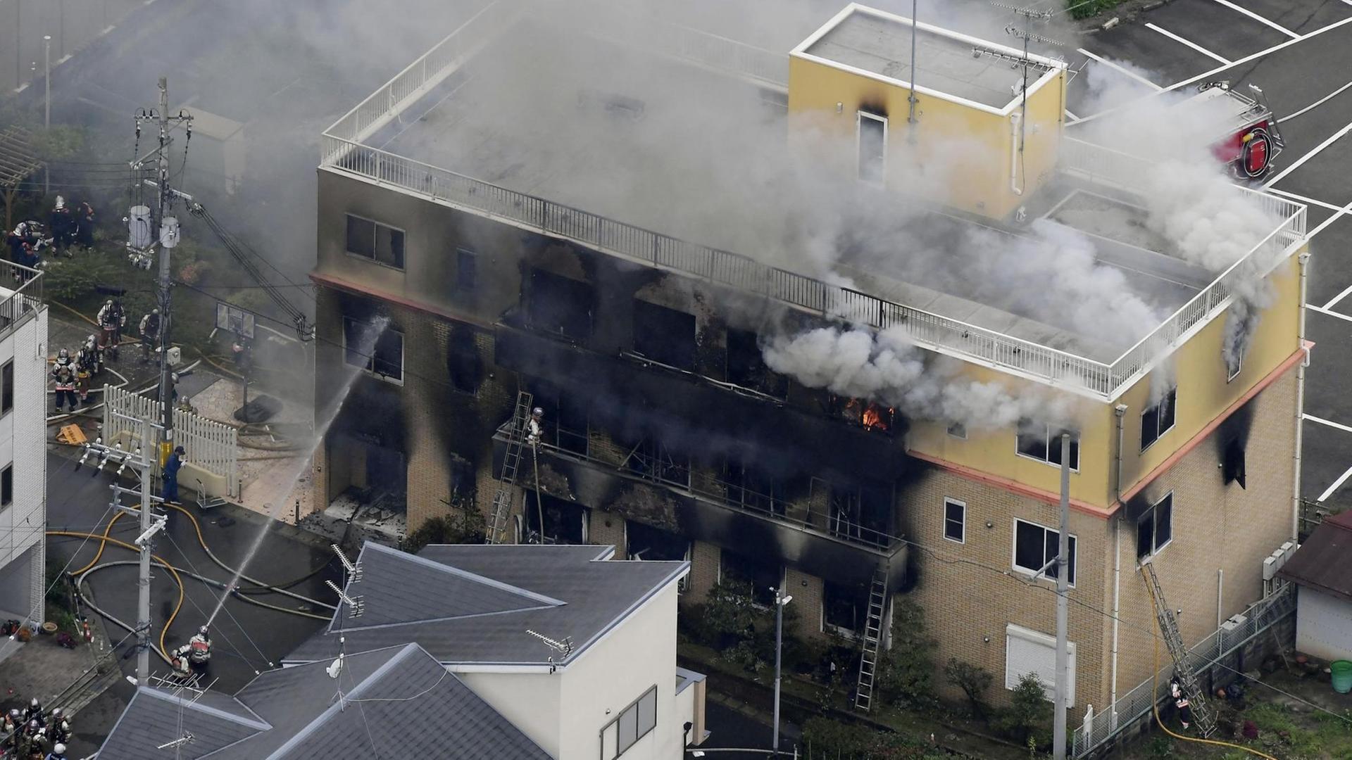 Blick von schräg oben auf das brennende und verkohlte Gebäude: Rauch und Flammen dringen aus allen Stockwerken. Feuerwehrleute spritzen Wasser durch die zerstörten Fenster. Blick von schräg oben auf das brennende und verkohlte Gebäude: Rauch und Flammen dringen aus allen Stockwerken. Feuerwehrleute spritzen Wasser durch die zerstörten Fenster.