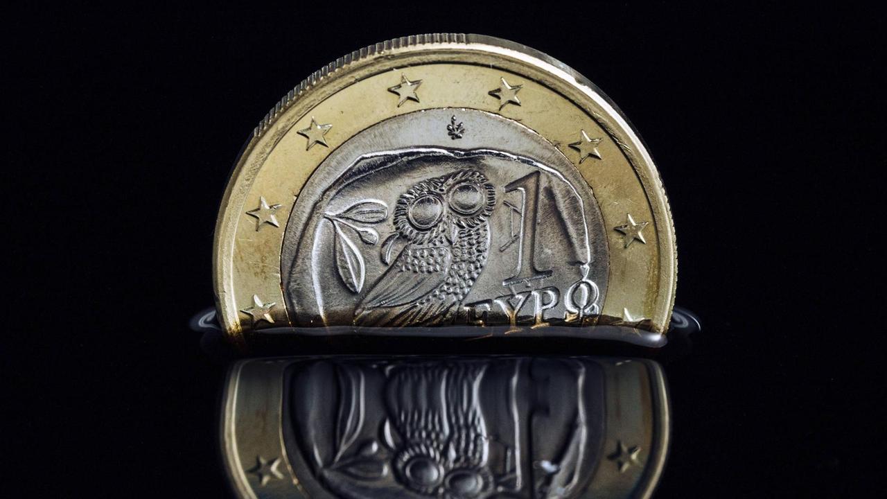 Die griechische Euro-Münze versinkt in schwarzer Flüssigkeit.