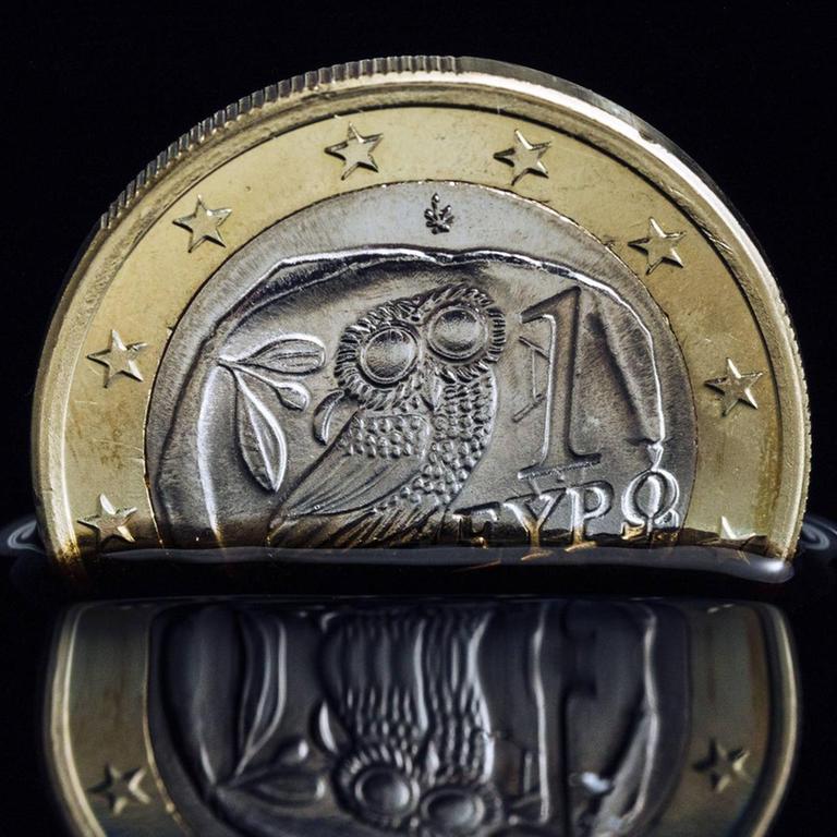 Die griechische Euro-Münze versinkt in schwarzer Flüssigkeit. 
