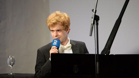 Der Pianist Alexej Gorlatch sitzt an einem Flügel auf der Bühne und hält ein DLF-Mikrofon in den Händen