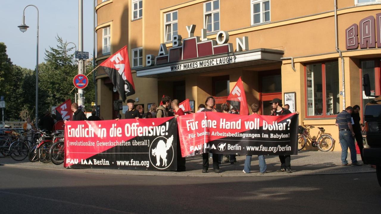 Eine Gruppe Menschen mit rot-schwarzen Transparenten steht vor dem Berliner Kino "Babylon", Auf den Transparenten sind das Logo der "FAU" und die Aufschrift: "Endlich in die Offensive - revolutionäre Gewerkschaften überall"
