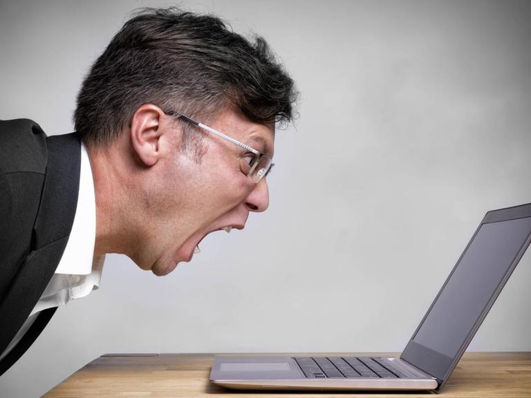 Ein Mann schreit sein Laptop an.
