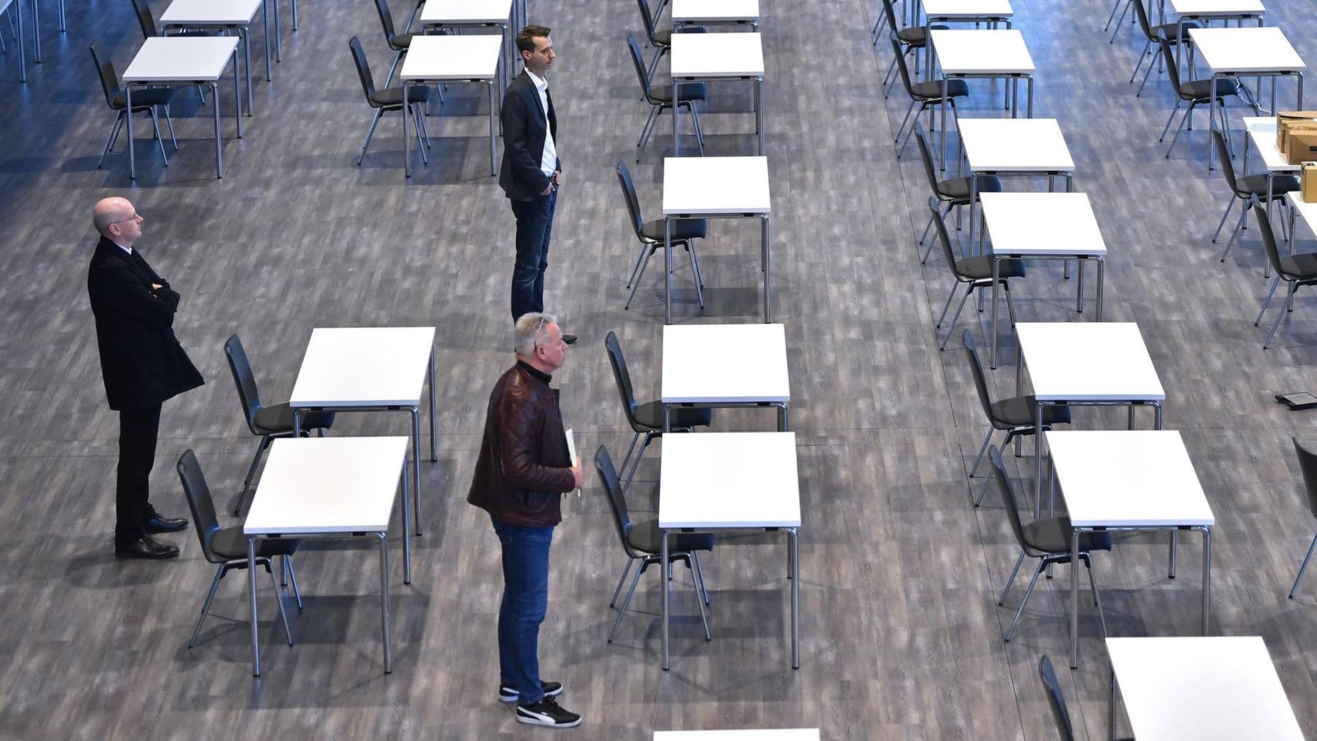 Drei Thüringer Landtagsmitarbeiter besichtigen einen Saal mit Tischen und Stühlen.