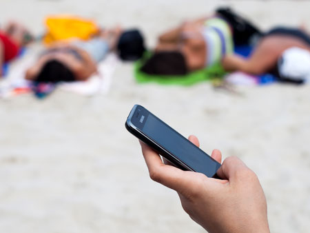Ein Smartphone liegt in der Hand eines Urlaubers am Strand.