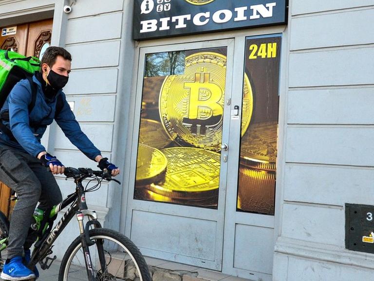 Ein Radfahrer mit Mundschutz fährt an einem Bitcoin-Wechsel-Laden in Krakau vorbei.