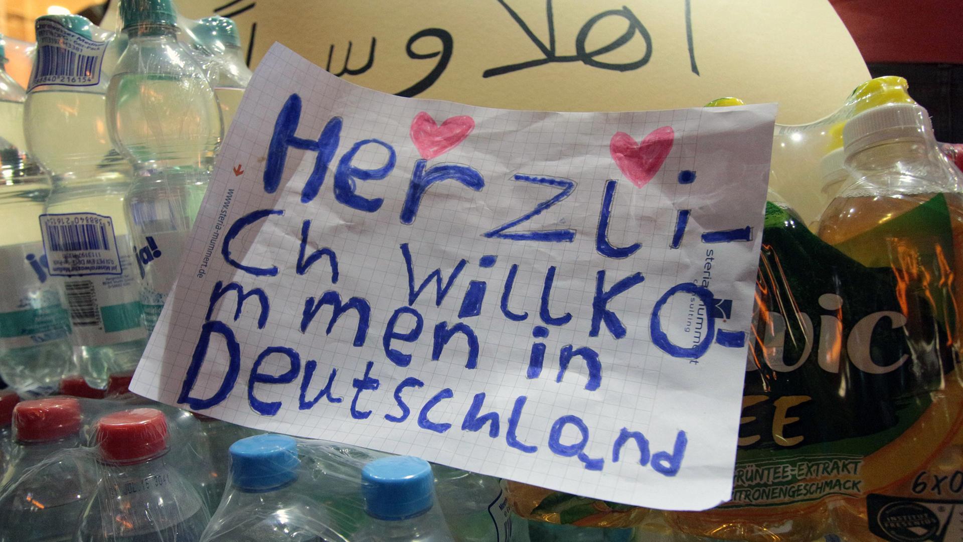 "Herzlich Willkommen in Deutschland" steht mit zwei Herzchen in Kinderschrift auf einem Zettel zwischen Wasserflaschen