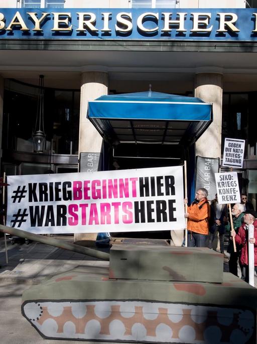 Demonstranten vom Aktionsbündnis "Gegen die Münchner Sicherheitskonferenz" stehen am 15.02.2017 mit Plakaten und einem Panzer aus Pappe vor dem Hotel "Bayerischer Hof".