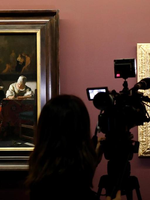 Sie sehen einen Journalisten, der das Gemälde "Briefschreiberin und Dienstmagd" von Vermeer filmt.