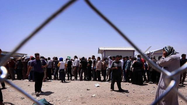 Hinter einem Maschendrahtzaun stehen auf staubigem Boden dichtgedrängt Dutzende Flüchtlinge.