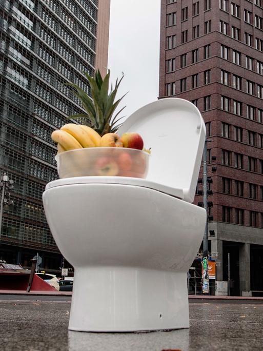 Eine Toilette mit einem Obstkorb steht auf einem großen Platz.