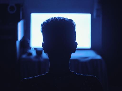 Ein Mann sitzt in einem dunklen Raum vor einem hell erleuchtenden Monitor.