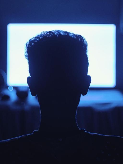 Ein Mann sitzt in einem dunklen Raum vor einem hell erleuchtenden Monitor.