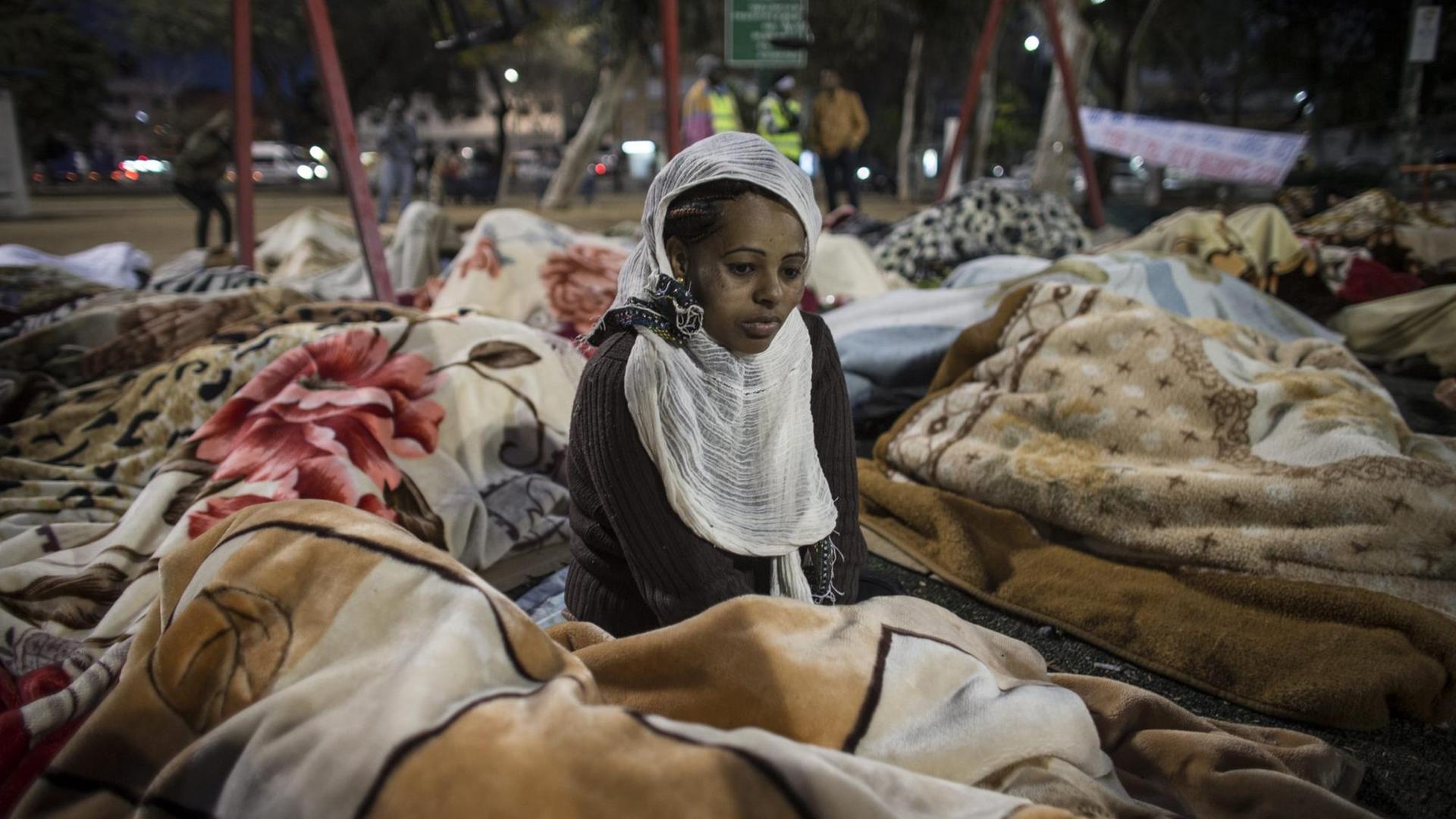 Eritreische Geflüchtete in Tel Aviv: Auf dem Boden sitzend, in Decken gewickelt.