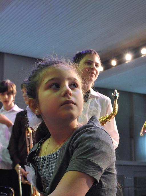 Ein Mädchen am Klavier hört einem Jungen beim Saxofon-Spielen zu.