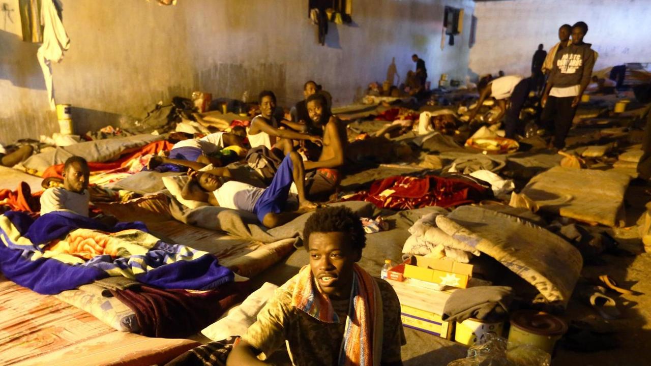 Afrikanische Geflüchtete in einem Lager in Tripolis in Libyen. Sie liegen auf dem Boden auf Matten. Keine Fenster, dicht an dicht.