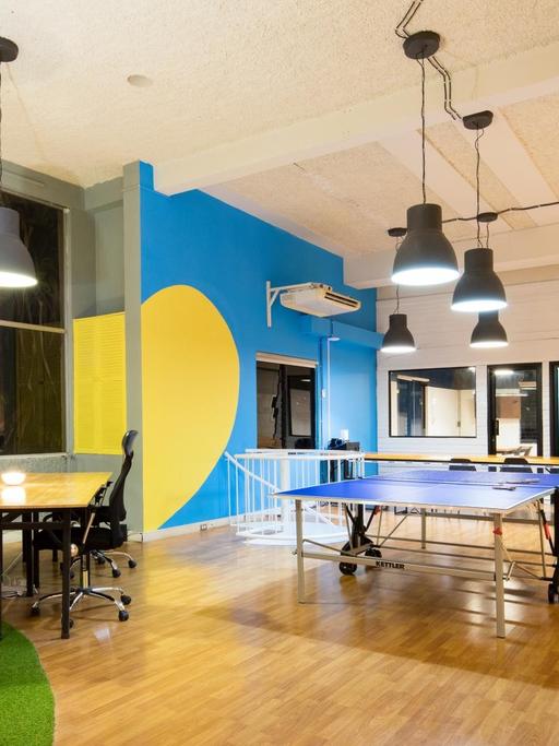 Aufnahme eines Startup-Büros. Mitten im Raum steht eine Tischtennisplatte. An der Seite Sitzgelegenheiten und eine Bar.