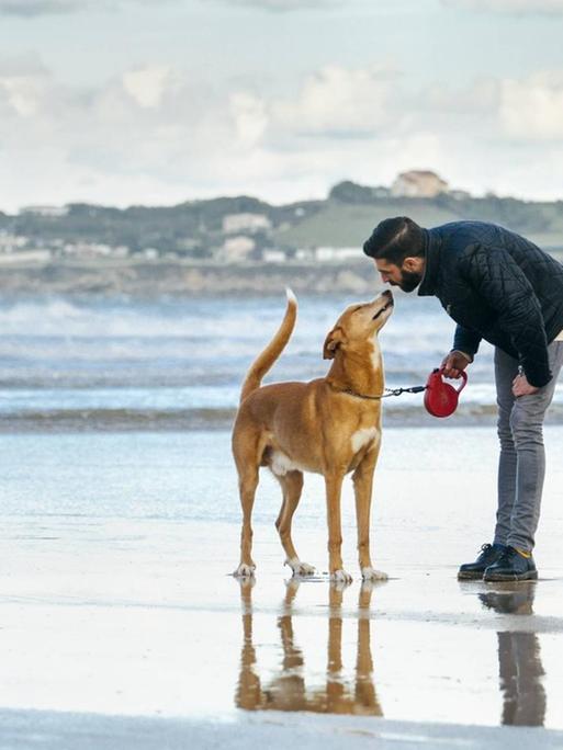Ein Mann mit einem Hund am Strand.