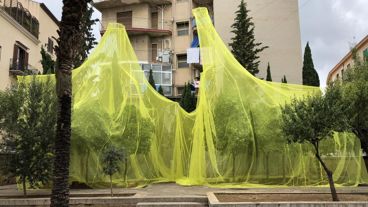 Gelbe Netze hängen über Bäumen auf einem Platz in Palermo