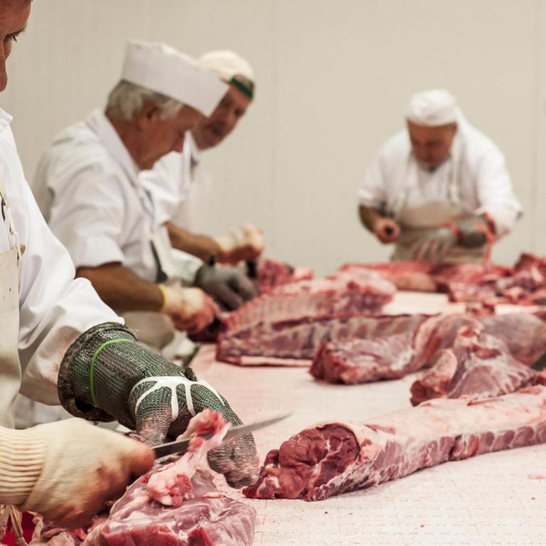 Arbeiter verarbeiten Fleisch in einem Schlachtbetrieb. 