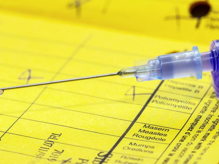 Ein gelber Impfpass mit einer Spritze mit dem Impfpfstoff gegen Masern in Nahaufnahme.