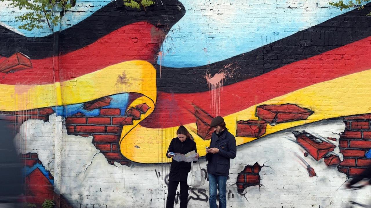 Passanten stehen an einem Wandbild mit der deutschen Nationalflagge.