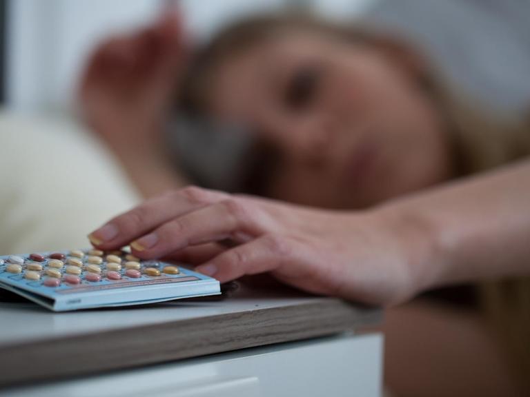 Eine Frau greift am nach ihrer Pille, die auf dem Nachtschrank liegt