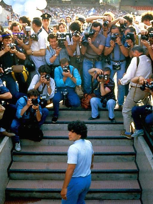 Im Still aus "Diego Maradona" steht der Fußballspieler von Fotografen umringt auf einer Treppe.