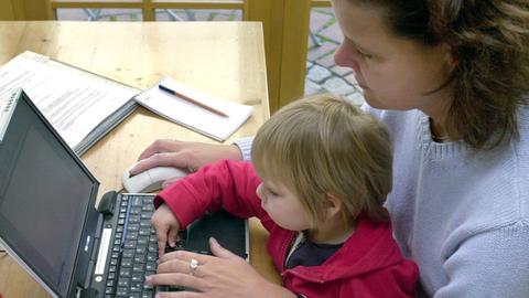 Eine Mutter versucht mit ihrem Kind auf dem Schoß an einem Laptop zu arbeiten.