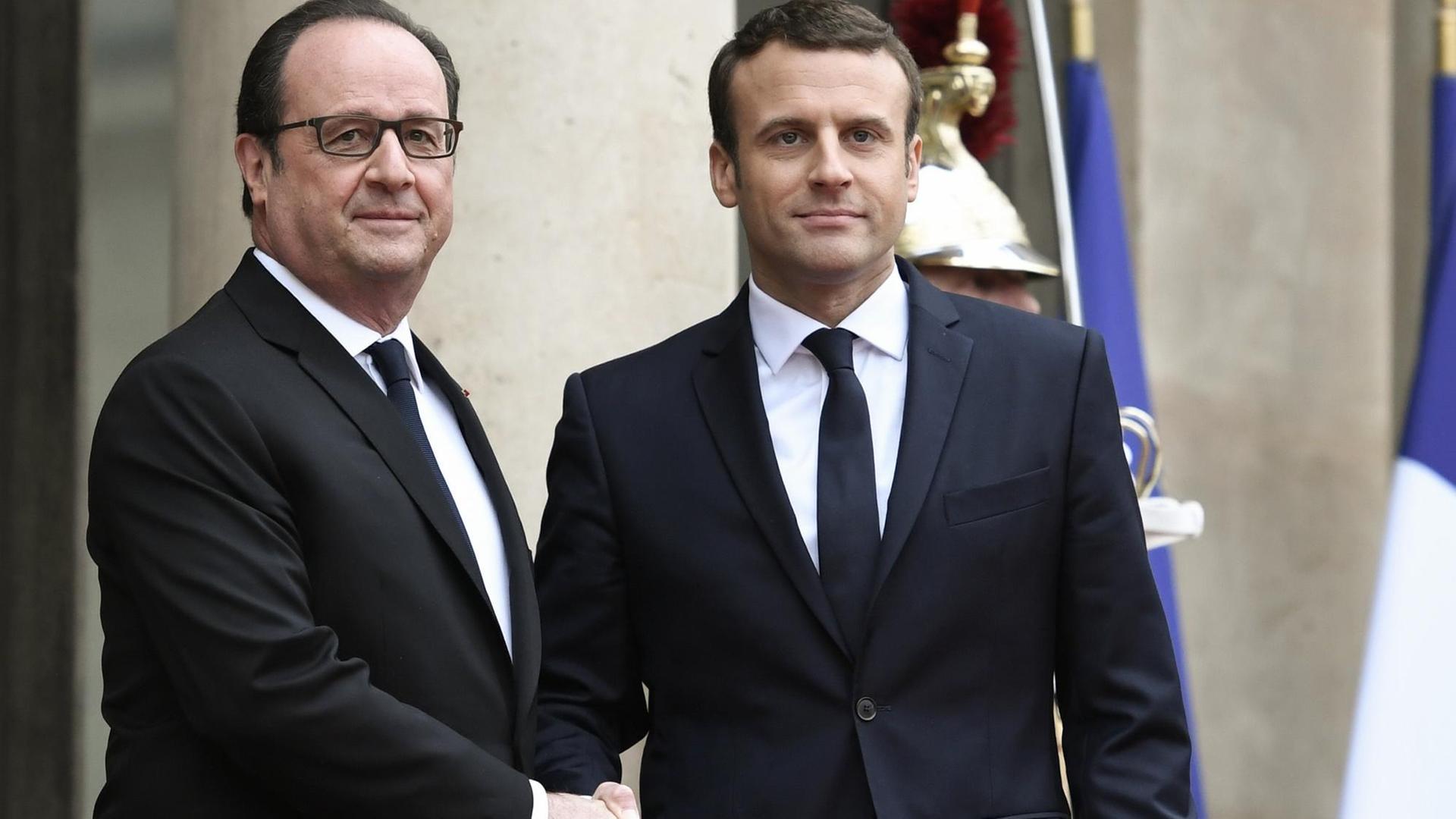 Francois Hollande begrüßt seinen Amtsnachfolger Emmanuel Macron am14. Mai 2017 im Elysée-Palast. Die beiden schütteln sich die Hände und lächeln in die Kameras.