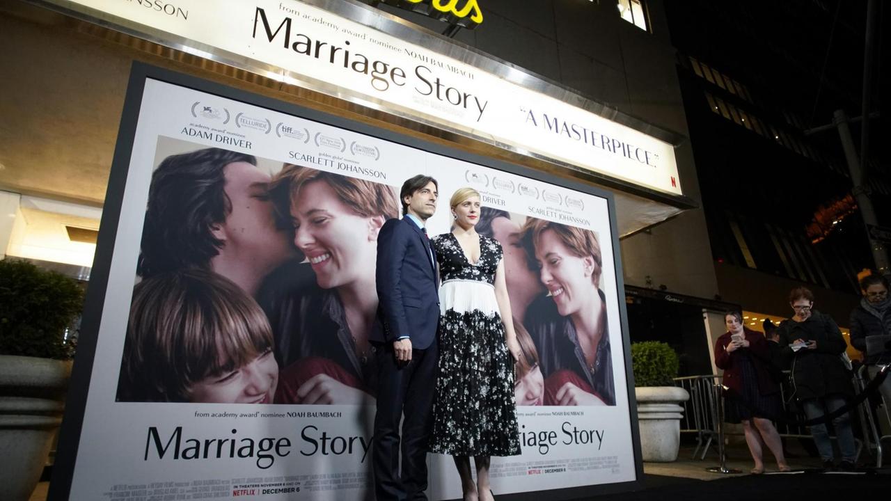 Regisseur Noah Baumbach und seine Frau Greta Gerwig stehen auf einem dunklen Teppich. Hinter Ihnen ist das übergroße Filmplakat von "Marriage Story" zu sehen.