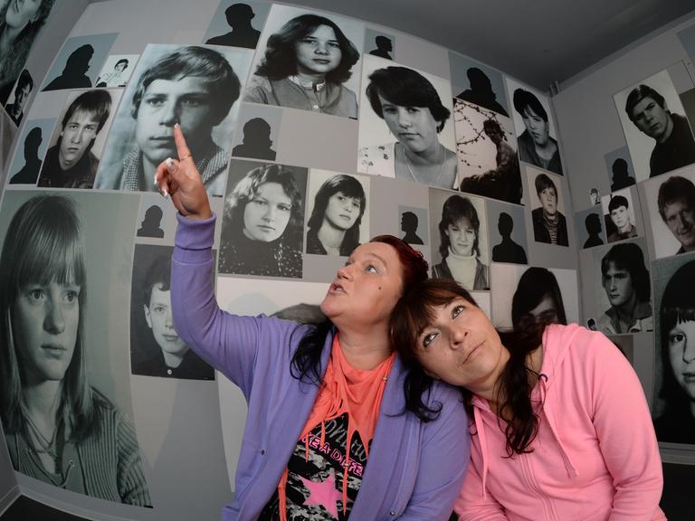 In einem Raum mit Porträtfotos sitzen Jana Mendes Bogas (l) und Ilona Dothe am 14.09.2013 auf einem Treffen ehemaliger DDR-Heimkinder in der "Gedenkstätte Geschlossener Jugendwerkhof" in Torgau (Sachsen).