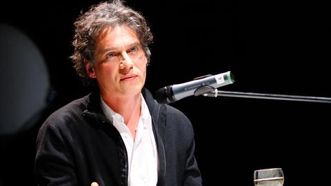 Der Autor Holger Siemann bei einer Lesung sitzend am Tisch mit einem Mikrofon.