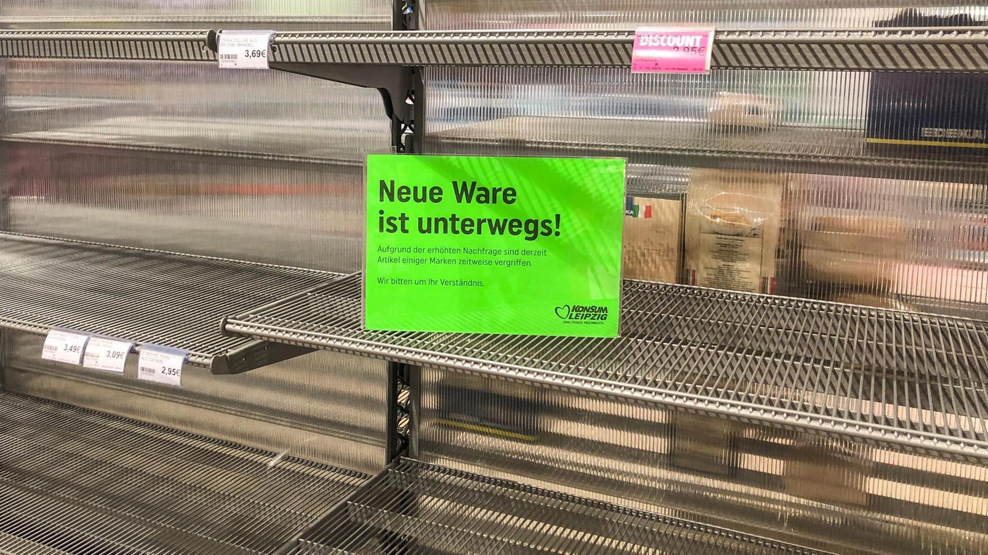 Ein Schild mit der Aufschrift "Neue Ware ist unterwegs!" ist an einem leeren Supermarkt-Regal angebracht, in dem ursprünglich Toilettenpapier stand.