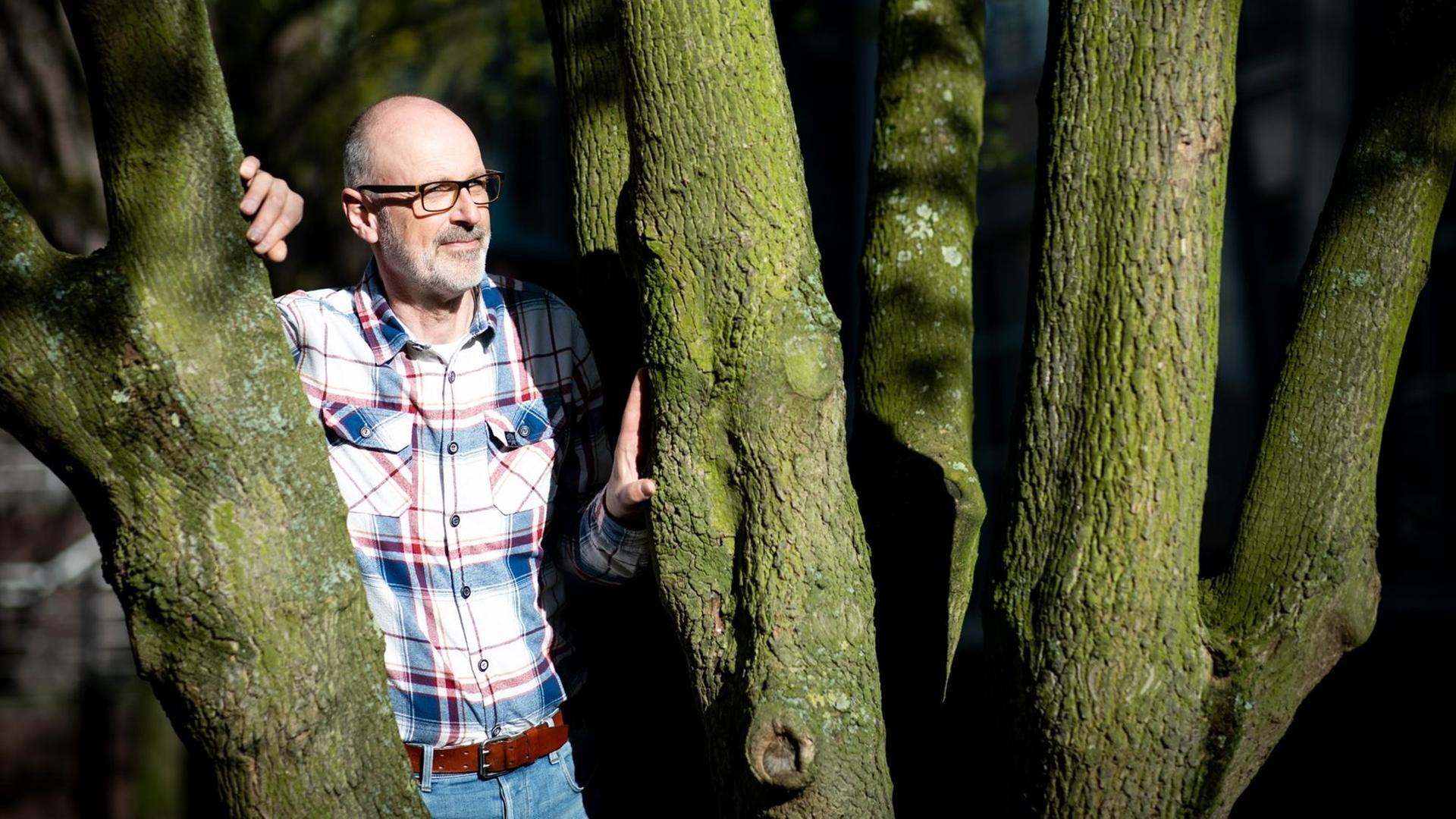 Das Foto zeigt den Förster und Bestseller-Autor Peter Wohlleben, wie er zwischen zwei Bäumen steht.