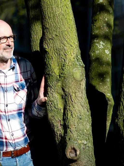 Das Foto zeigt den Förster und Bestseller-Autor Peter Wohlleben, wie er zwischen zwei Bäumen steht.