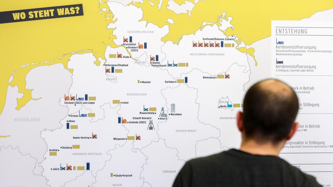 Ein Mann steht vor einer Deutschlandkarte, auf der Daten zur Atommüll-Endlager-Suche verzeichnet sind.